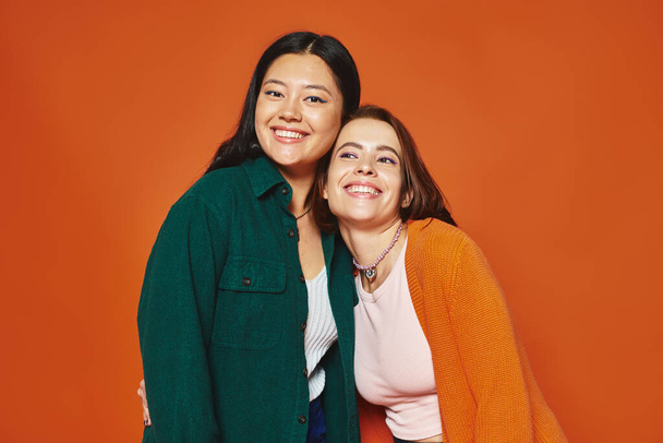 strahlende und multikulturelle Freundinnen, die einen freudigen Moment auf warm orangefarbenem Hintergrund teilen, Vielfalt - Foto, Bild