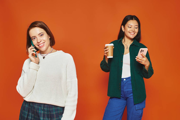 iloinen ja nuori monikulttuurinen naiset käyttävät älypuhelimia ja seisoo oranssi tausta - Valokuva, kuva