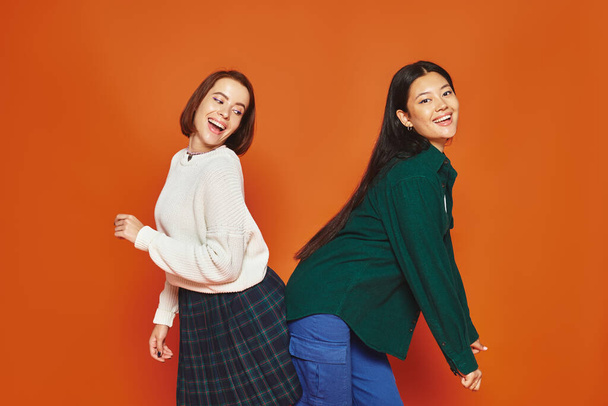 felici giovani donne multiculturali in vivace abbigliamento casual divertirsi su sfondo arancione, amicizia - Foto, immagini