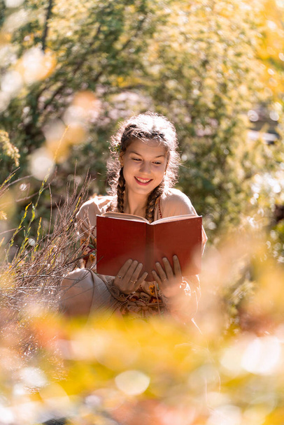jonge vrouw glimlachen terwijl genieten van het lezen van een boek buiten in de natuur. - Foto, afbeelding