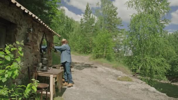 Sehr lange Aufnahme eines reifen Menschen, der am Tisch vor dem Haus im Wald steht und seinen Arbeitsplatz organisiert - Filmmaterial, Video