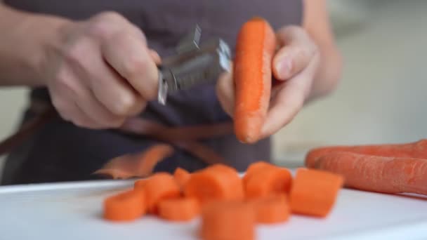 figura mulher irreconhecível em avental marrom descascando cenouras com faca de descascar na cozinha - Filmagem, Vídeo