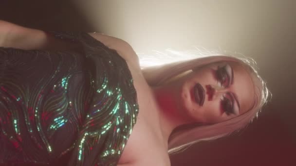 Függőleges közepes portré magabiztos kaukázusi drag queen fényes ruhában pózol kamera alatt reflektorfényben - Felvétel, videó
