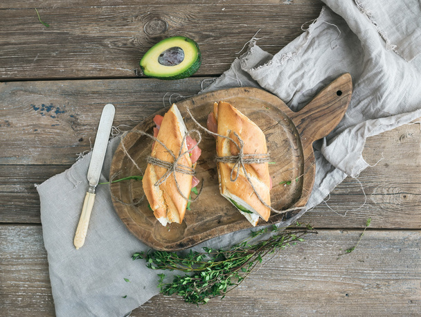 Salmon, avocado and thyme sandwiches in baguette tied up with decoration rope on a rustic wooden board over rough wood background - Zdjęcie, obraz