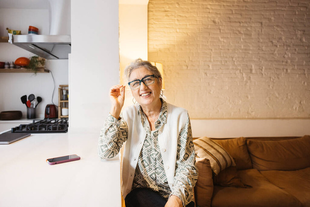 Portrait de femme âgée souriante avec des lunettes dans le salon de sa maison. - Photo, image