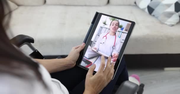 Pyörätuolissa istuva nainen kommunikoi lääkärin kanssa etänä kotoa tabletin videopuhelun kautta. Vammaisten etälääketiede - Materiaali, video