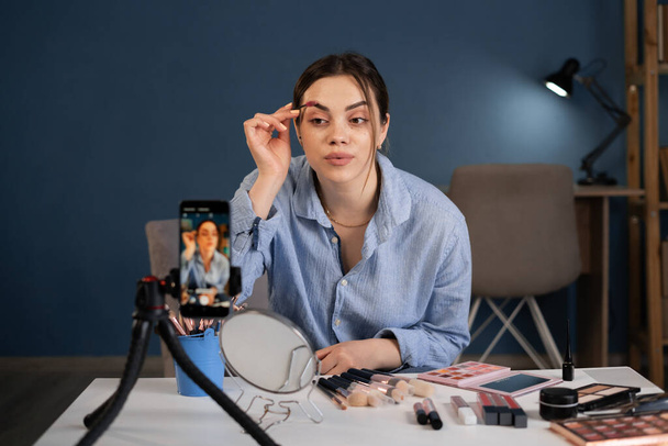 Beauty blogger κορίτσι μαγνητοσκόπηση καθημερινή make-up ρουτίνα φροντιστήριο στην κάμερα smartphone. Influencer κορίτσι live streaming καλλυντικά προϊόν αναθεώρηση στο στούντιο στο σπίτι. Αντιγραφή χώρου - Φωτογραφία, εικόνα
