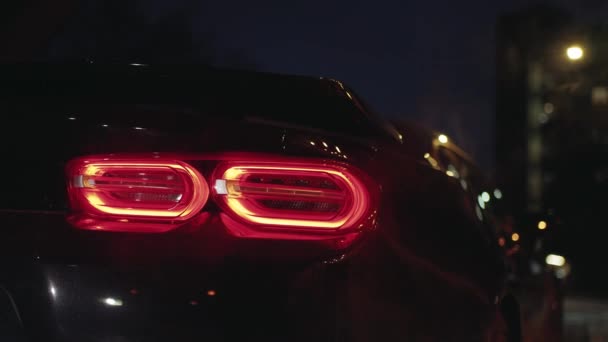 Czarne sportowe tylne światło samochodu świecące w ciemności nocnego miasta, migające światło parkingowe - Materiał filmowy, wideo