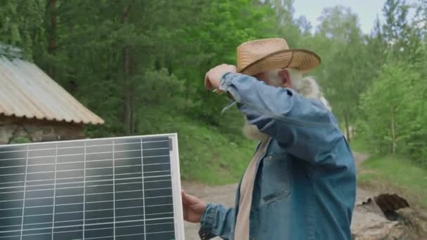 Vue latérale du pensionné portant un chapeau attrapant les courants de lumière du soleil tout en plaçant le panneau solaire à l'extérieur - Séquence, vidéo