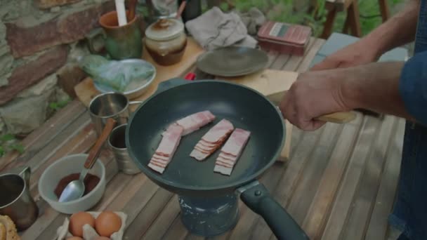 Plan recadré d'un homme méconnaissable cuisinant le petit déjeuner avec du bacon à la cuisine extérieure - Séquence, vidéo