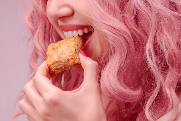 Femme aux cheveux bouclés roses mange du baklava gros plan. - Photo, image
