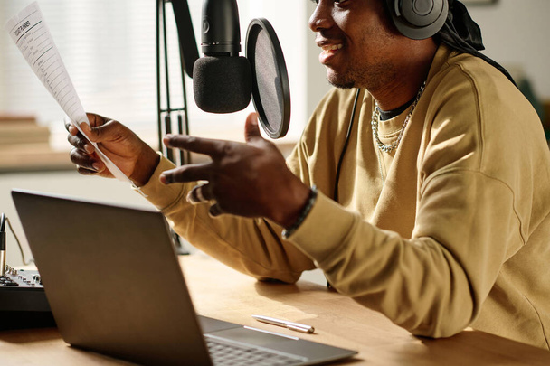 Fokus auf Papier in der Hand eines jungen afroamerikanischen Bloggers oder Radiomoderators, der während der Sendung Text im Mikrofon liest - Foto, Bild