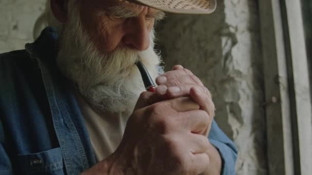 Gros plan d'un homme barbu âgé portant un chapeau fumant tout en se reposant à l'intérieur - Séquence, vidéo