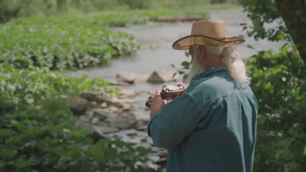 Medium long shot of elderly person taking photos of river while traveling to forest - Footage, Video