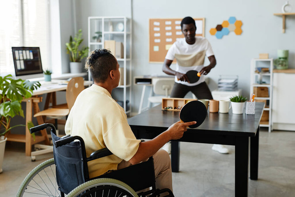 Achteraanzicht bij jonge vrouw met een handicap die tafeltennis speelt op kantoor, inclusiviteit op de werkplek concept - Foto, afbeelding