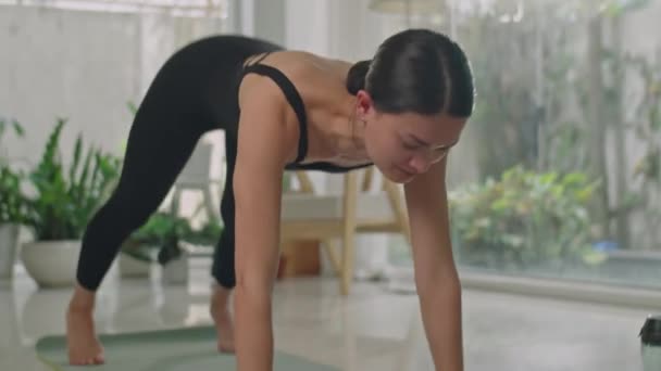 Mujer joven en traje deportivo haciendo flujo de vinyasa yoga mientras hace ejercicio en casa durante el día - Metraje, vídeo