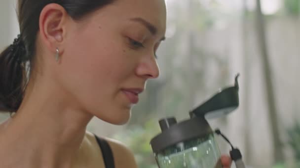 Крупним планом молода жінка п'є воду зі спортивної пляшки, маючи перерву під час домашніх тренувань - Кадри, відео