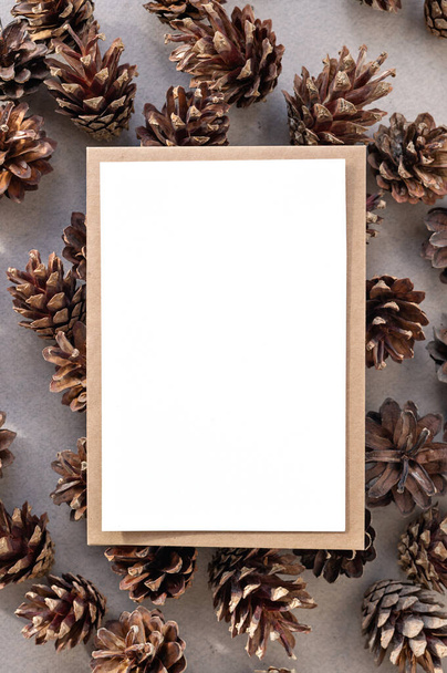 Aesthetic natural rustic Christmas card mockup with copy space, blank paper card background and envelope on pine cones background. Elegant winter invitation, postcard, business branding template. - Photo, Image