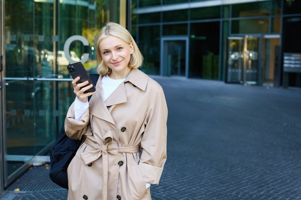 Ritratto di giovane donna elegante che cammina nel centro della città con smartphone, usando l'app per cellulare all'aperto, aspettando qualcuno, andando al lavoro. - Foto, immagini