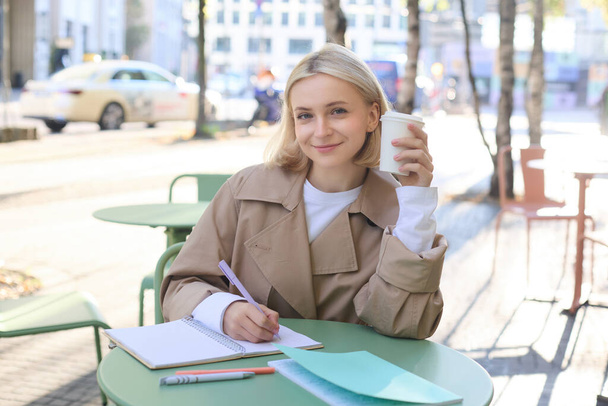 Gülümseyen genç bir kadın resmi, kadın girişimci yazısı, dokümanlarda düzeltmeler yapan, defter kullanan, kahve içen ve açık hava kafede oturan.. - Fotoğraf, Görsel