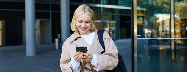 Porträt einer jungen, stylischen Frau, die mit dem Smartphone in der Innenstadt spazieren geht, die Handy-App im Freien nutzt, auf jemanden wartet, zur Arbeit geht. - Foto, Bild