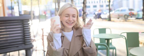 陽気な若いブロンドの女性の肖像画は,屋外カフェで時間を過ごし,コーヒーを飲んで笑い,ストリートレストランでカジュアルに会う. ライフスタイルコンセプト - 写真・画像