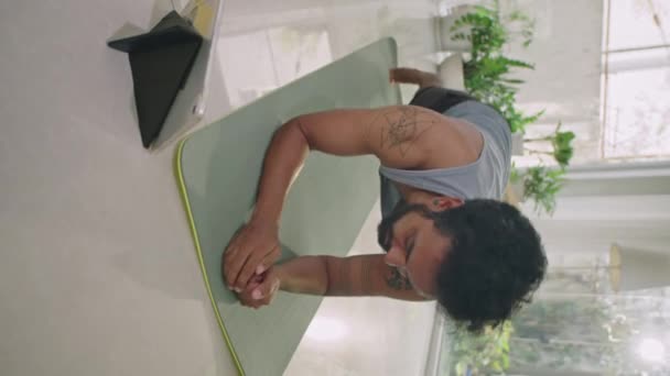 Függőleges lövés atlétikai férfi csinál deszka tornaterem és nézni videó edzés digitális tabletta edzés közben otthon - Felvétel, videó