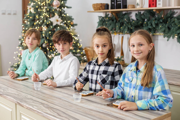 I bambini di gruppo disegnano vernici alimentari sui biscotti di pan di zenzero fatti in casa di Natale. Concetto Natale. - Foto, immagini