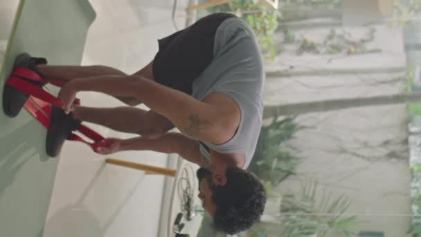 Tiro vertical de homem esportivo realizando agachamentos com banda de resistência no tapete de exercício na sala de estar durante o treino em casa - Filmagem, Vídeo