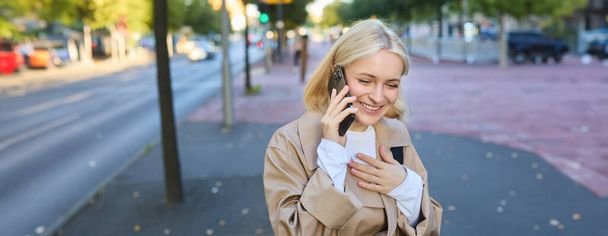 Κοντινό πλάνο πορτρέτο του χαρούμενου κοριτσιού που γελάει, στέκεται στο δρόμο με το smartphone, μιλώντας στο κινητό τηλέφωνο, γελώντας και χαμογελώντας. Έννοια ανθρώπων - Φωτογραφία, εικόνα