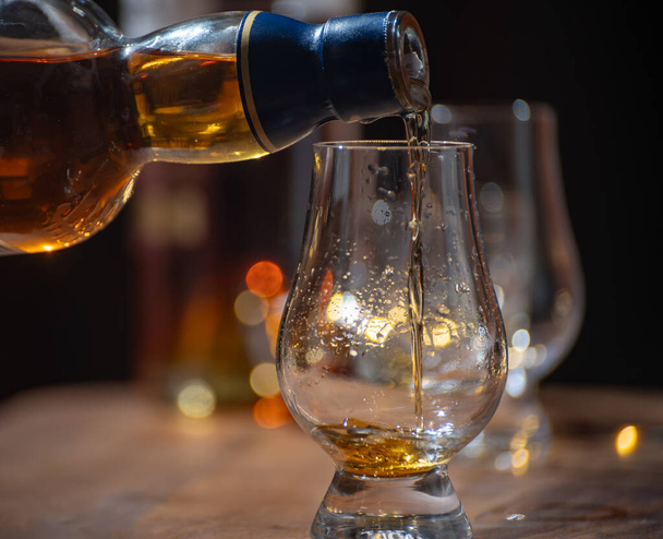 Pouring of whisky, glasses of single malt and blended scotch whisky served in bar in Edinburgh, Scotland, UK with party lights on background - Photo, Image