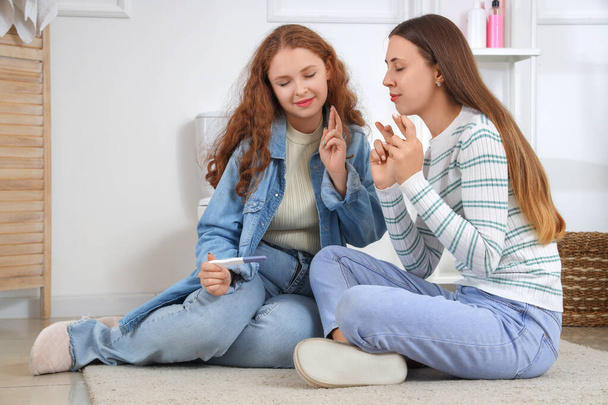 Young lesbian couple with pregnancy test crossing fingers in bathroom - Foto, Imagem