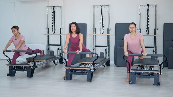 Three Asian women in pink sportswear do exercises on the reformer machine. Pilates classes - Foto, afbeelding