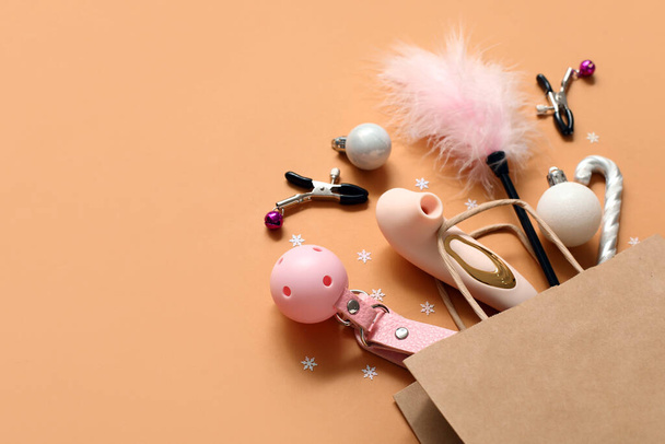 Bolsa de compras con diferentes juguetes sexuales y decoración de Navidad sobre fondo naranja - Foto, Imagen