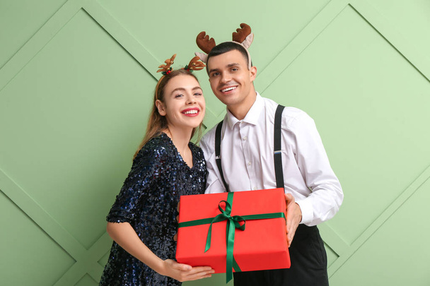 Mooi jong paar in rendieren hoorns met kerst geschenkdoos op groene achtergrond - Foto, afbeelding