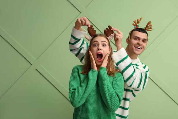 Beautiful young couple in reindeer horns on green background - Фото, зображення
