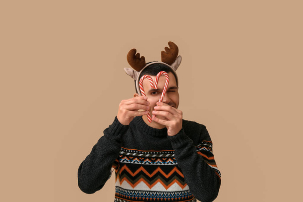 Geyik boynuzlu genç adam bej arka planda Noel şekerleri kamışlarıyla - Fotoğraf, Görsel