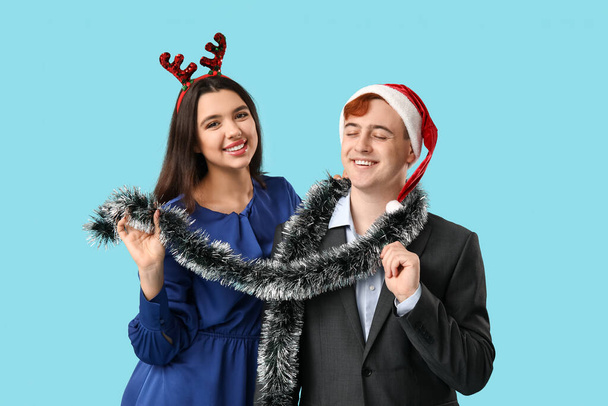 Happy young couple with Christmas tinsel on blue background - Photo, Image