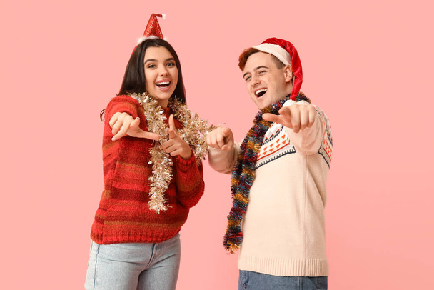 Feliz casal jovem em chapéus de Papai Noel com ouropel de Natal no fundo rosa - Foto, Imagem