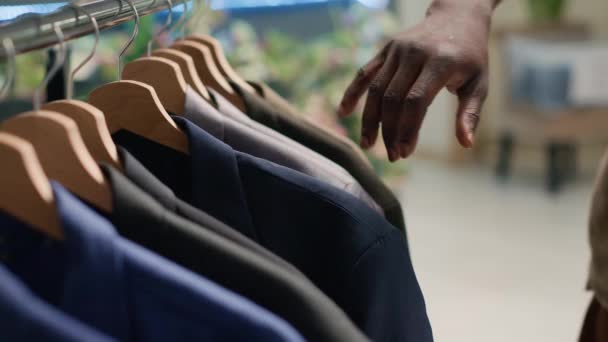 Πελάτης σε κατάστημα μεταχειρισμένων περιήγηση μέσα από τα ρούχα στις σχάρες για να βρείτε τέλεια στολή. Κοντινό πλάνο του πελάτη στο κατάστημα μεταχειρισμένων ειδών ένδυσης κάνει ψώνια, θέλοντας να αγοράσει κομψό σακάκι - Πλάνα, βίντεο