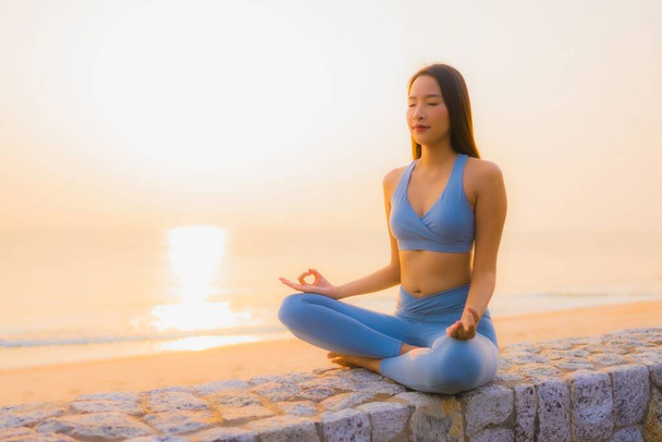 肖像若いアジアの女性は健康のために日の出に海のビーチの海の周りに瞑想を行う - 写真・画像