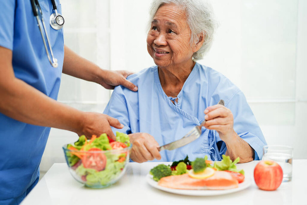 Aziatische oudere vrouw patiënt eten zalm staak en groente salade voor gezond voedsel in het ziekenhuis. - Foto, afbeelding