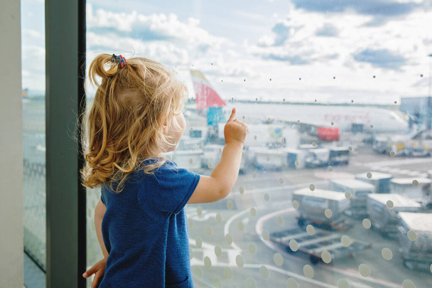 Jolie petite fille tout-petit à l'aéroport, voyageant. Heureux enfant en bonne santé attendant près de la fenêtre et regardant les avions. Famille en vacances d'été en avion - Photo, image