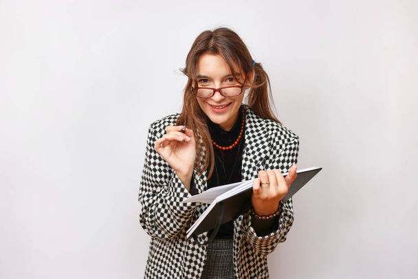 Ένας φοιτητής με γυαλιά κάνει μια σημείωση σε ένα σημειωματάριο. Η διαδικασία των σπουδών στο πανεπιστήμιο. - Φωτογραφία, εικόνα
