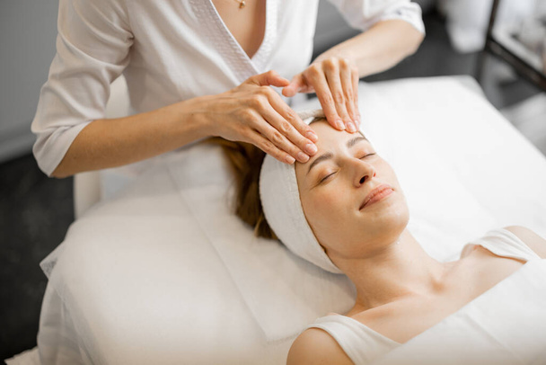 Kosmetička provádí profesionální masáž obličeje pro ženy v salonu krásy. Mladá dospělá běloška dostává relaxační masáž obličeje - Fotografie, Obrázek