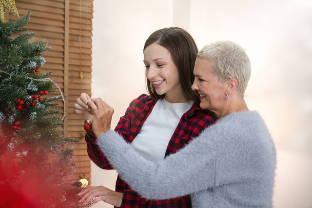 Moeder en dochter zijn enthousiast en blij om de kerstboom thuis te versieren tijdens de feestdagen. Tijd samen doorbrengen met Kerstmis. - Foto, afbeelding