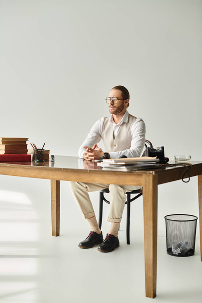 aantrekkelijke jongeman met baard en bril met verzamelde haar zitten aan tafel in zijn kantoor - Foto, afbeelding