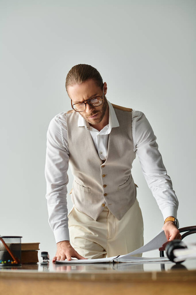 elmélkedő jóképű férfi szemüveggel és szakállal nézi jegyzeteit munka közben az irodában - Fotó, kép