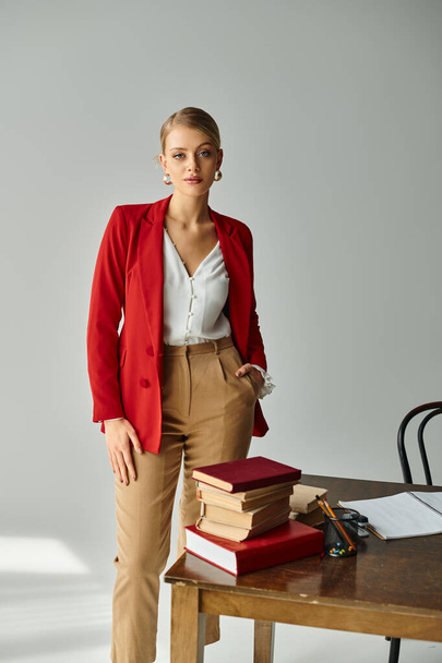 гарна молода жінка в червоній куртці позує з рукою в кишені і дивиться на камеру в офісі - Фото, зображення