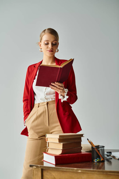 alluring woman with blonde hair in vivid attire reading next to pile of books with hand in pocket - Photo, Image